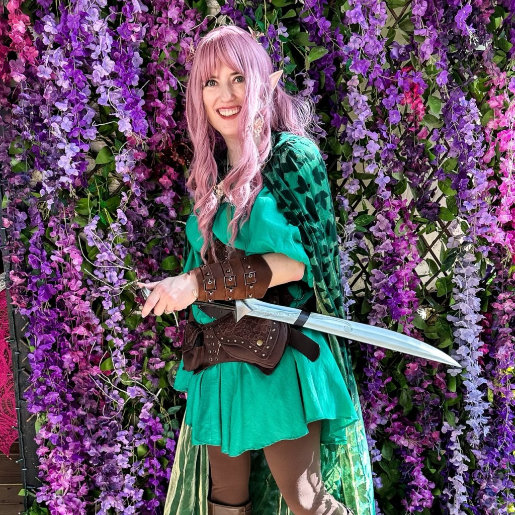 Texas Renaissance Festival Outfit - A girl dressed like an elf with a pink hair, a green dress, brown boots, and an elven sword.